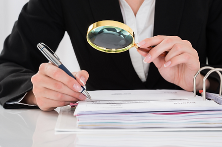 Person reviewing documents with a magnifying glass and pen