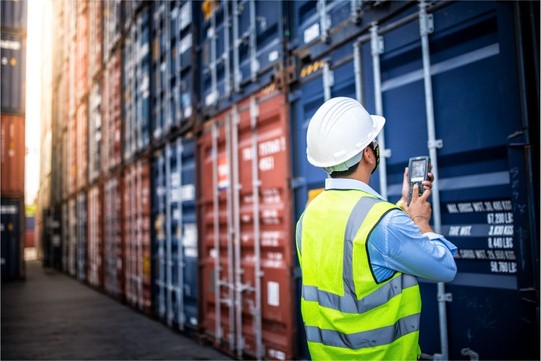 Customs officer in a hard hat checking shipping containers at a port